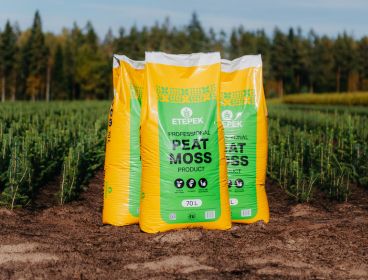 Three yellow and green bags of ETEPEK professional peat moss product standing on soil in an outdoor field with green trees and plants in the background.