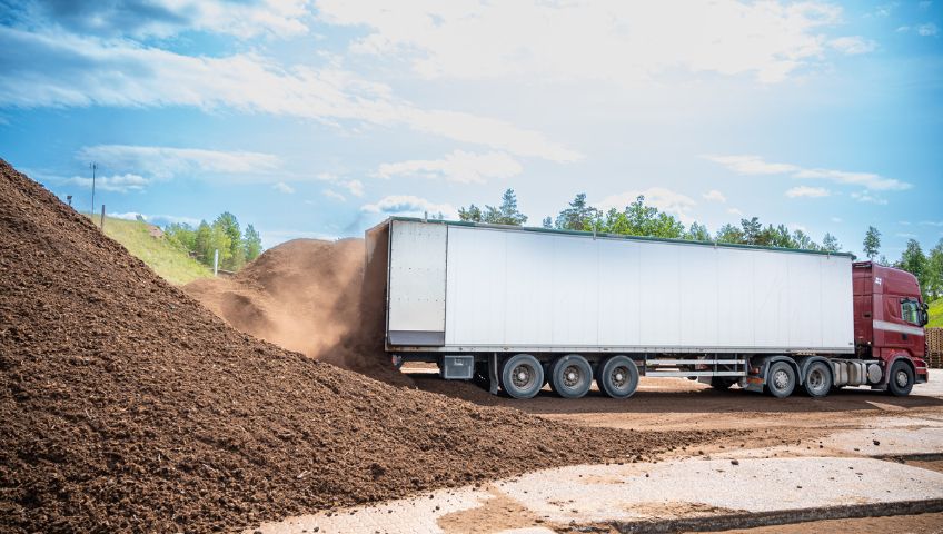 A large truck unloading a pile of ETEPEK's organic peat moss in an open outdoor facility, with a clear blue sky and greenery in the background.