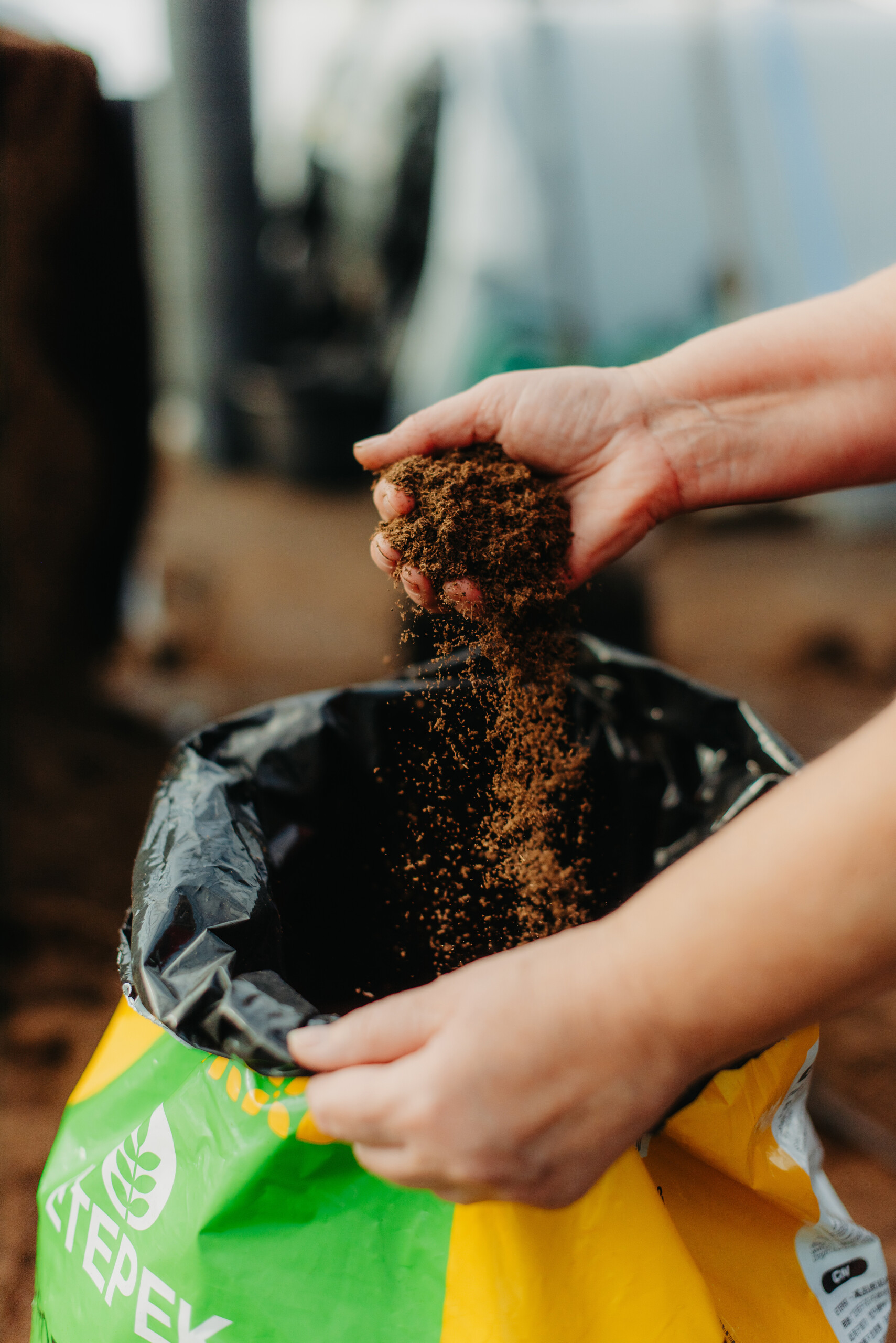 Close-up of hands sifting peat moss into an ETEPEK-branded bag, showcasing the product's texture and quality.