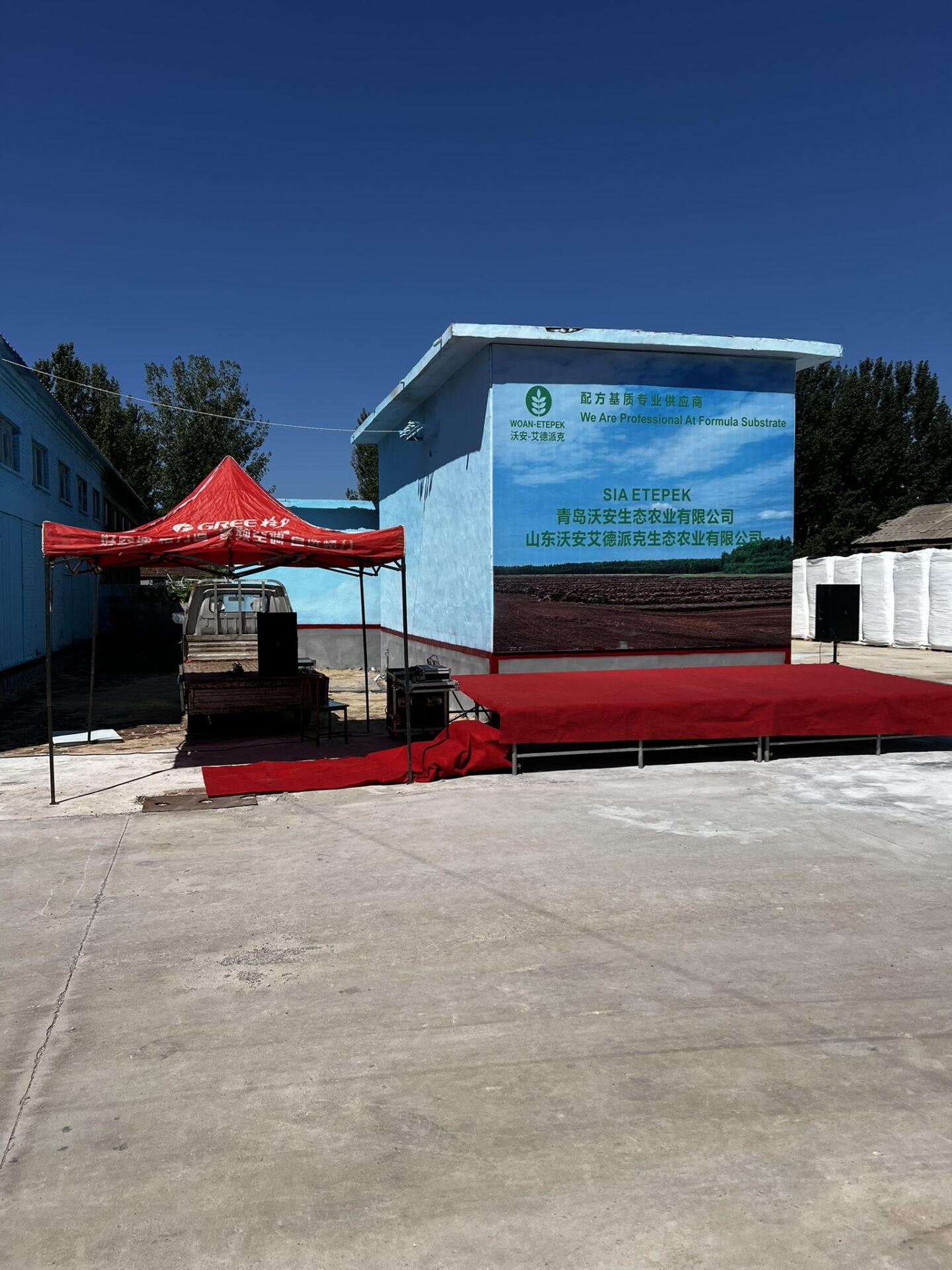 A promotional setup with a red canopy and stage in front of a building featuring the WOAN-ETEPEK logo and branding, located in China.